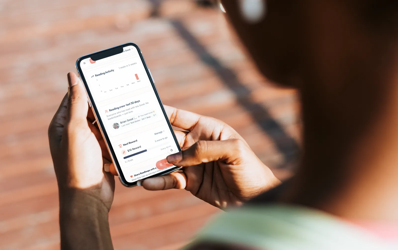 Hands holding a phone showing the Readloops dashboard with reading activity and next reward